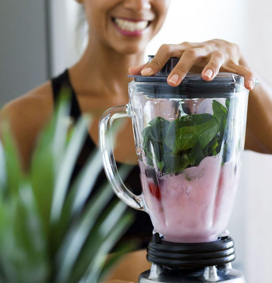 Frischer grüner Smoothie in einem Glas, umgeben von frischen Zutaten wie Spinat, Banane, Beeren und einem Löffel Sooperfood-Pulver – perfekt für einen gesunden Start in den Tag.